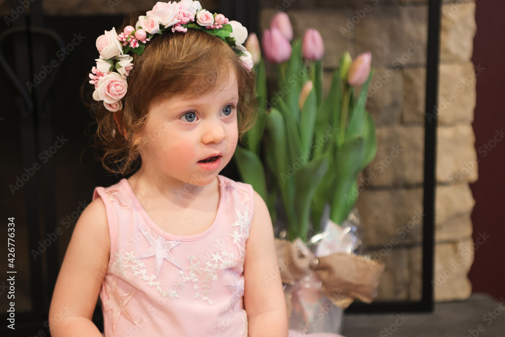 Close Up Portrait, 2 Years Old Toddler Girl with Big Blue Eyes, in light Pink Dress with Pink Flowers on her head, Sitting by the fireplace, Birthday Girl, Ukrainian Head bend, Little Princess 