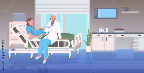 doctor in uniform using stethoscope examining pregnant woman lying in hospital bed before childbirth gynecology consultation pregnancy concept full length horizontal