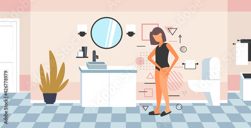 woman testing skin presence of stretch marks checking cellulite on her buttock girl clamping fat fold on hip diet weight loss concept bathroom interior full length horizontal