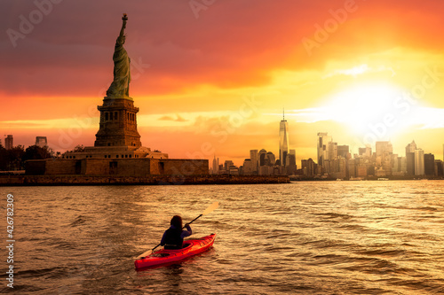 Adventurous Woman Sea Kayaking near the Statue of Liberty. Colorful Sunrise sky Art Render. Taken in Jersey City, New Jersey, United States. © edb3_16