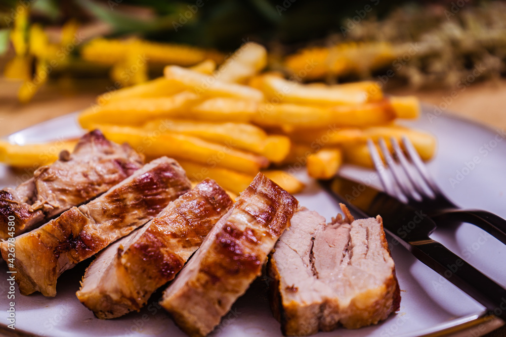 Grilled pork breast cut into strips on a plate with french fries.
