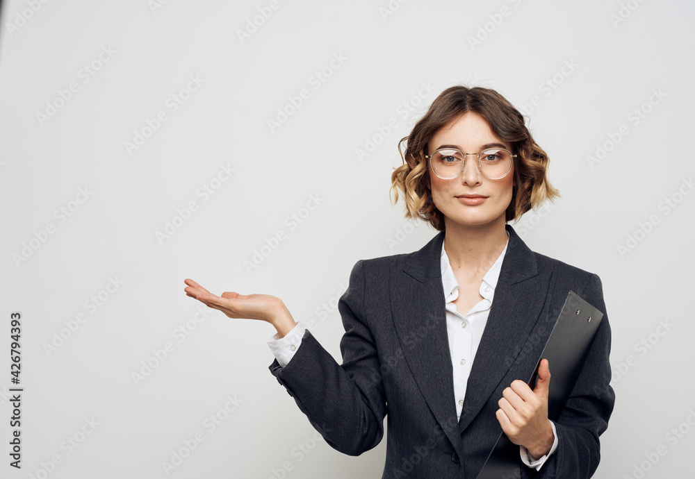Business woman with documents gestures with her hands on a light background and glasses on her face Business woman with documents gestures with her hands on a light background and glasses on her face
