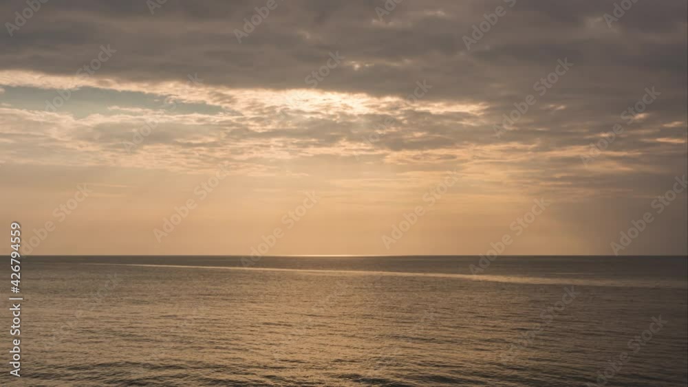 sunlight shines through dramatic gray clouds over the ocean. sunset at the horizon. beautiful ray sunbeams shine from heaven to the earth. sunlight reflected on seawater in very calm ocean waves. sunlight shines through dramatic gray clouds over the ocean. sunset at the horizon. beautiful ray sunbeams shine from heaven to the earth. sunlight reflected on seawater in very calm ocean waves.