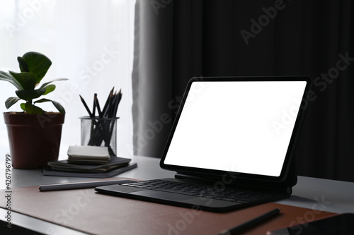Computer tablet with blank screen, house plant and pencil holder on home office desk.
