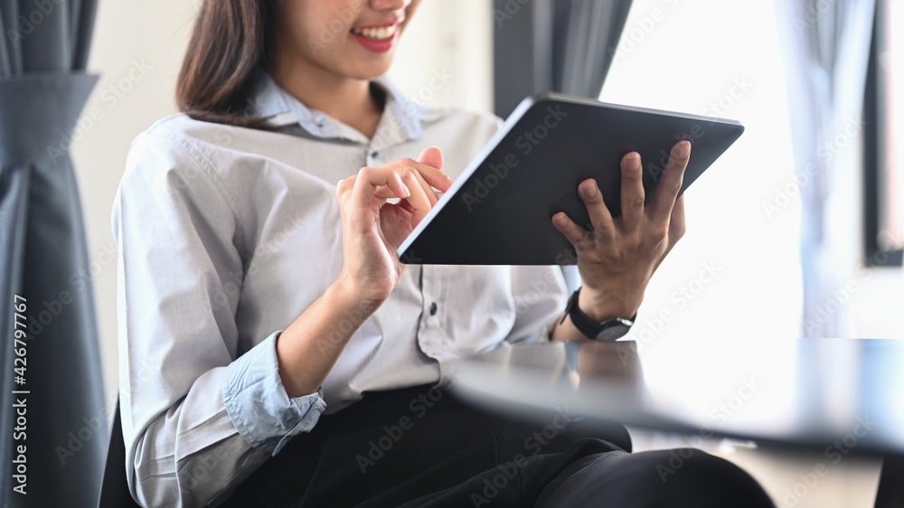 Cropped shot of smiling young woman employee sitting in office and using digital tablet.