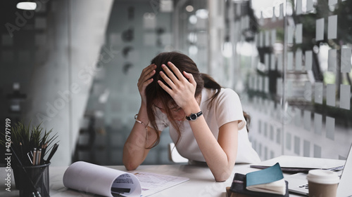 Fotografie Businesswoman sitting in her workplace and holding head with hands feeling desperate or suffers from headache