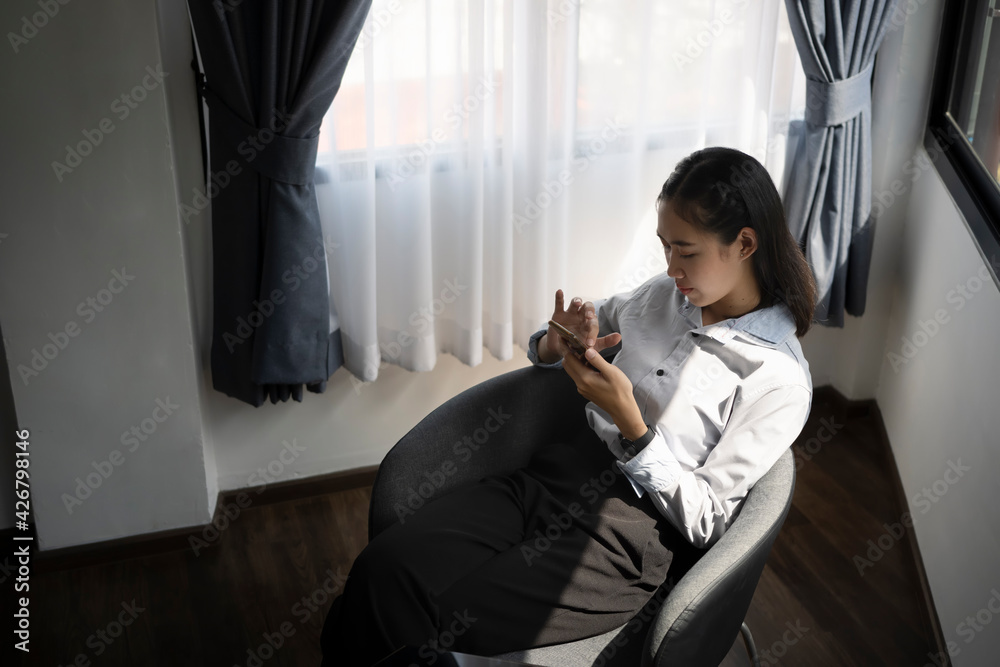Casual young asian woman sitting on comfortable chair and using smart phone.