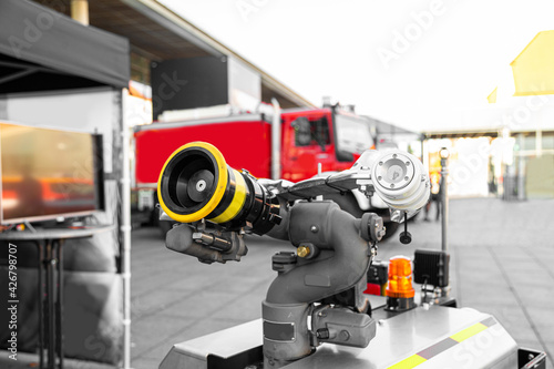 Modern high-tech firefighting robot with a hose for penetration into especially dangerous areas and extinguishing fires near red fire truck. Technology, transport and robotics concept