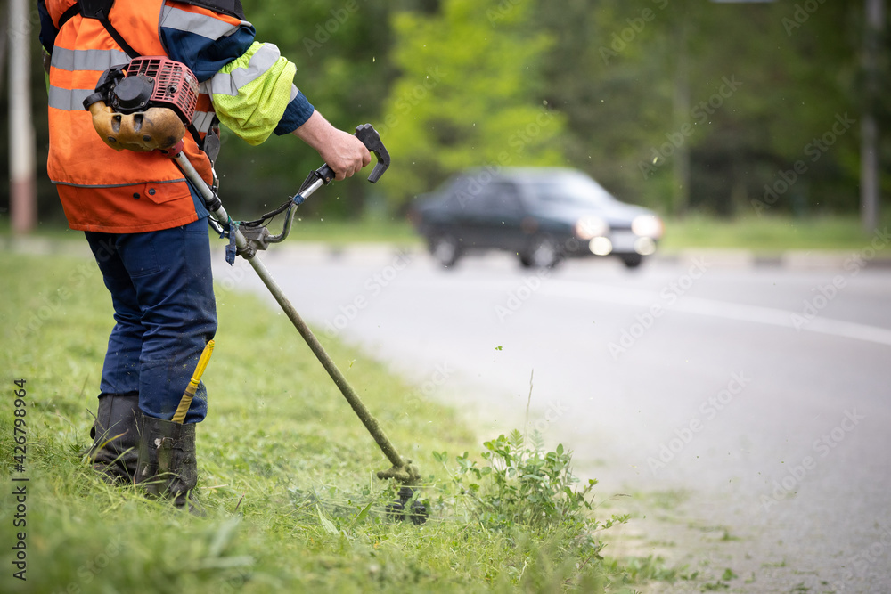 Closeup of a man with a lawn mower in his hands. A worker mows the grass on the side of the road. Improvement of the adjacent territory Closeup of a man with a lawn mower in his hands. A worker mows the grass on the side of the road. Improvement of the adjacent territory