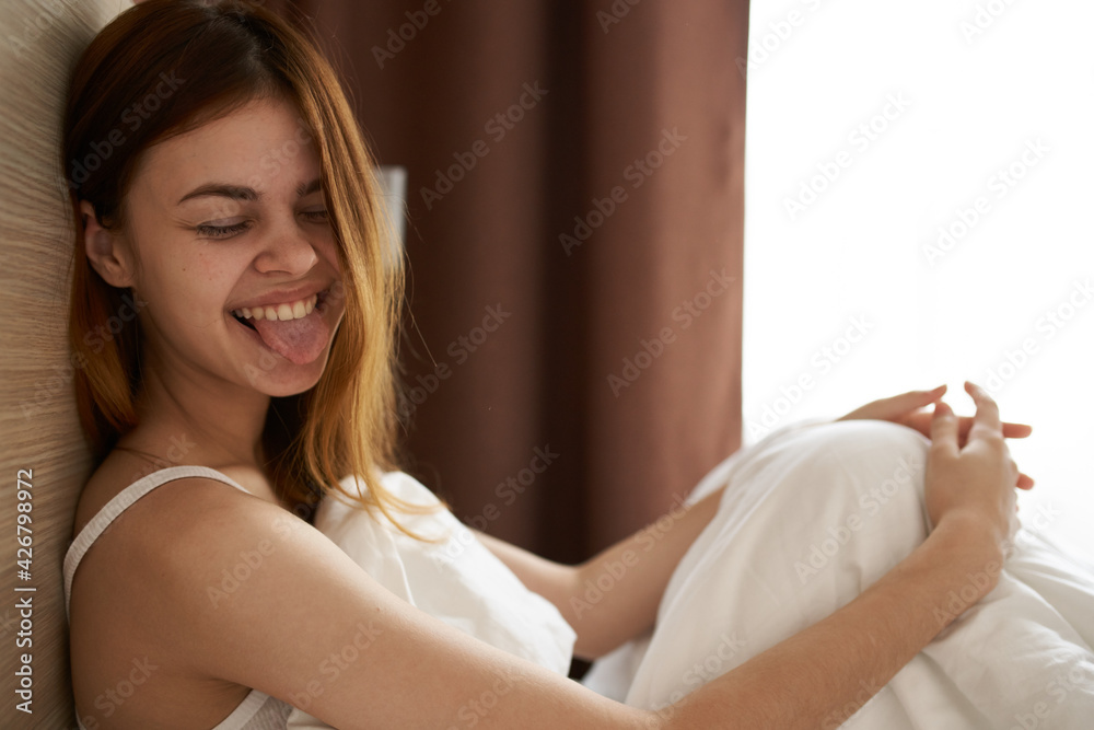 Fototapeta premium emotional woman lies in bed under the covers and gestures with her hands near the Copy Space window