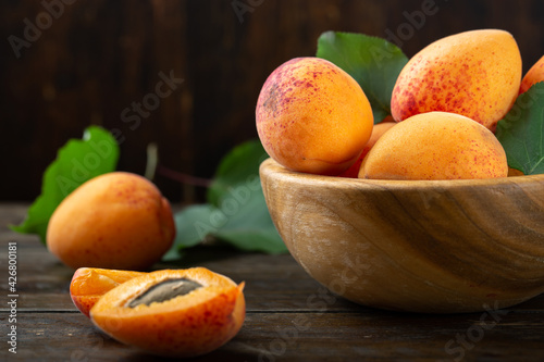 Ripe apricots and apricot leaves in a bowl on a wooden table. Fresh fruits from the home garden.