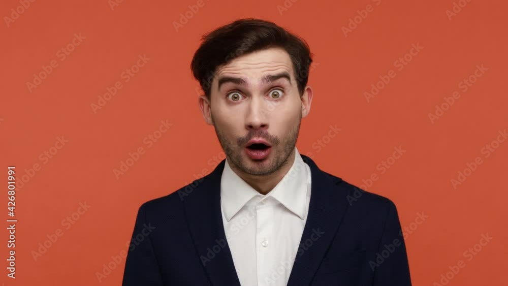 Oh my god, WOW. Bearded man wearing official style suit sees something astonishing and shocking, looks at camera with big surprised eyes. Indoor studio shot isolated on orange background. Oh my god, WOW. Bearded man wearing official style suit sees something astonishing and shocking, looks at camera with big surprised eyes. Indoor studio shot isolated on orange background.