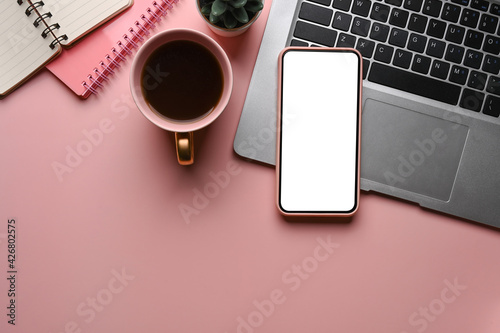 Top view of smart phone, laptop computer, notebook and coffe cup on pink background.