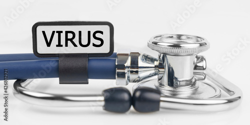 On the white surface lies a stethoscope with a plate with the inscription - VIRUS