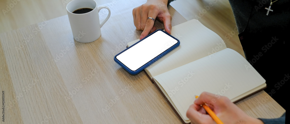 Cropped shot of man writing on empty notebook and using smart phone at home office. - obrazy, fototapety, plakaty 