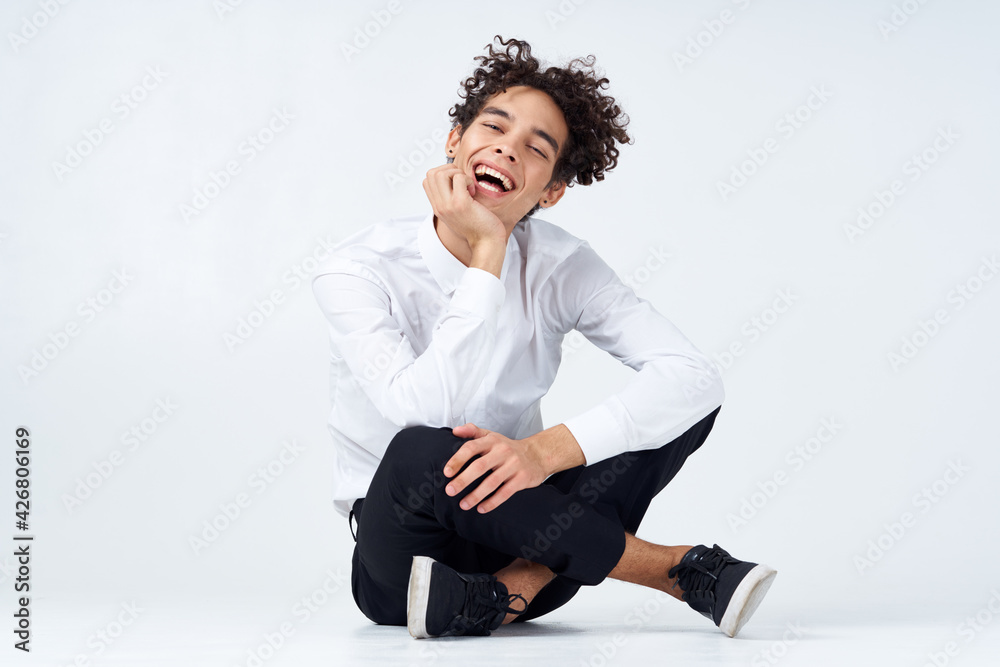 handsome young man with curly hair sits on the floor in a bright room with his legs crossed handsome young man with curly hair sits on the floor in a bright room with his legs crossed