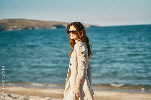 romantic woman in coat and t-shirt on the beach near the sea in the mountains