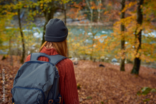 woman in a sweater with a backpack on her back near the river in the mountains and park trees autumn landscape