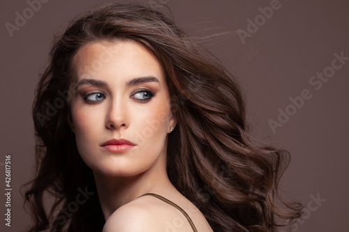 Portrait of attractive young woman with blowing long perfect dark hair on brown background