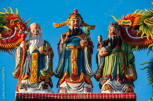 Vibrant colored statues of the three stellar gods of happiness and longevity, Fu Lu Shou, in Chinese mythology, contrasting with a deep blue sky. Tourist spot of Ishigaki island.