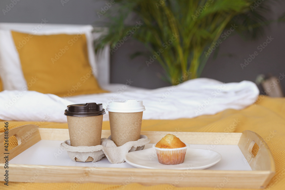 Two coffee cups and a cupcake on a white bed with an orange bedspread in a hotel bedroom banner. Romantic weekend for a couple with breakfast in bed on Valentine's Day. 