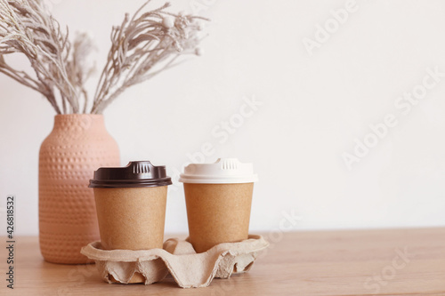 two paper cups with coffee and a cupcake on a table near a vase in a glass holder. breakfast for two. to be in love. take care of your partner. move to the guy. coffee for girlfriend