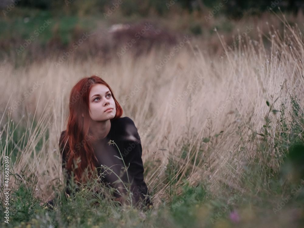 red-haired woman in a black dress lies in a field on dry grass in nature red-haired woman in a black dress lies in a field on dry grass in nature