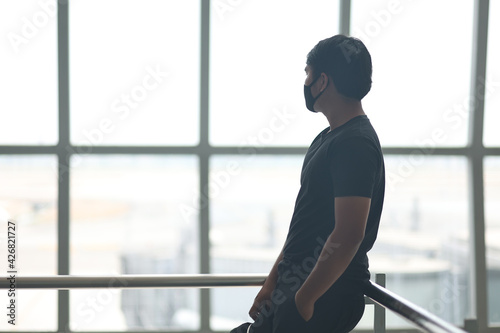Asian man wearing a mask stands on the ground of an airport in Bangkok, Thailand. The man in a black shirt wears a cloth mask to prevent infection.
