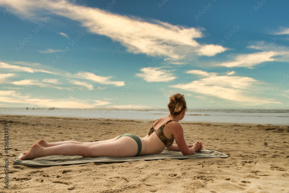 Beautiful woman in bikini sunbathing at the seaside. She lies on a green bath towel and looks at the sea while leaning on her hands Beautiful woman in bikini sunbathing at the seaside. She lies on a green bath towel and looks at the sea while leaning on her hands