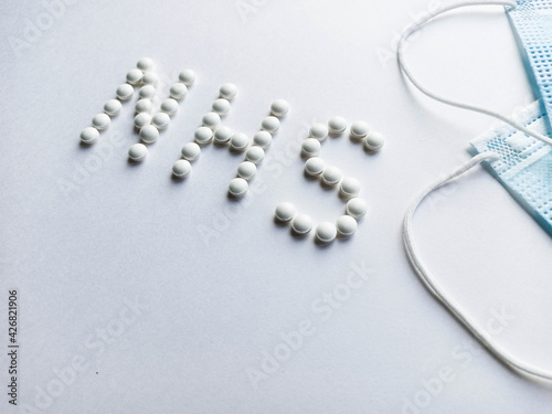 White pills in the form of an inscription nhs with medical masks.Medical protective mask isolated on white background. Healthcare medical Coronavirus quarantine, hygiene concept.