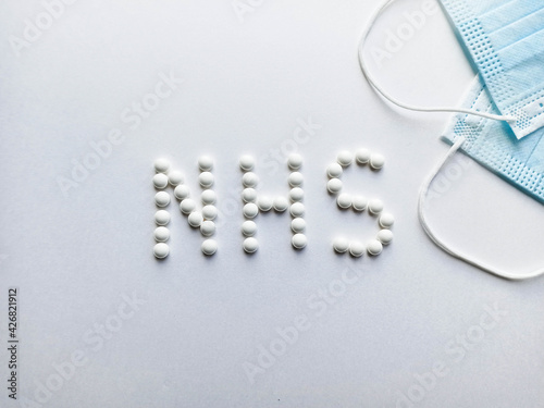 White pills in the form of an inscription nhs with medical masks.Medical protective mask isolated on white background. Healthcare medical Coronavirus quarantine, hygiene concept.