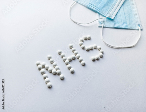 White pills in the form of an inscription nhs with medical masks.Medical protective mask isolated on white background. Healthcare medical Coronavirus quarantine, hygiene concept.