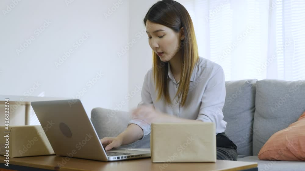 Asian woman writing the address on a cardboard box for after receiving online order preparing for delivery
