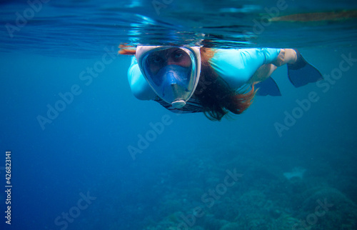Woman in full-face mask swimming in blue sea. Swimming in blue ocean water. Young woman swimming on sea surface. Snorkel in coral reef of tropical sea. Woman in snorkeling mask underwater photo