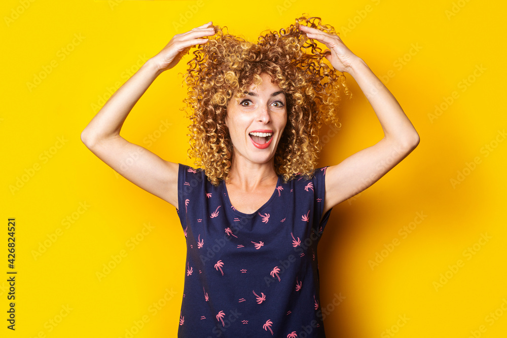 cheerful curly young woman lifts her hair up on a yellow background cheerful curly young woman lifts her hair up on a yellow background