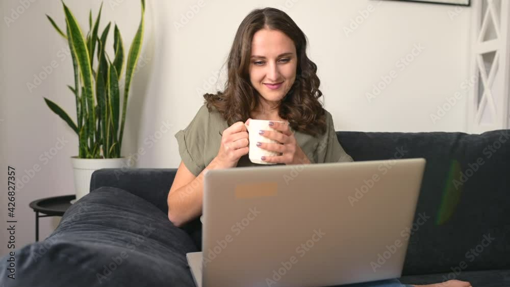 Female freelancer daydreaming with a cup of morning coffee, smiling woman sits on the couch with a laptop, looks away, waiting for inspiration or new ideas Female freelancer daydreaming with a cup of morning coffee, smiling woman sits on the couch with a laptop, looks away, waiting for inspiration or new ideas