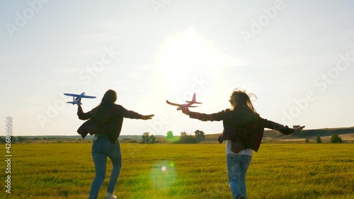Children on background of sun with an airplane in hand. Dreams of flying. Happy childhood concept. Two girls play with a toy plane at sunset. Silhouette of children playing on the plane