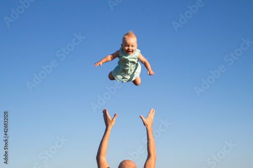 Man throws baby up against the blue sky. Concept game with children, happy family