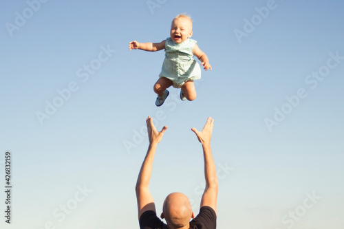 Dad throws his child up against the blue sky. Concept game with children, happy family