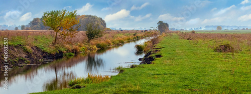 Narrow river among a wide field in the wild, autumn landscape, panorama