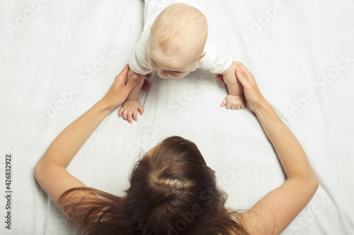 young mother teaches to crawl a little baby on the bed with a white sheet. Concept of education and child development. Flat lay, top view