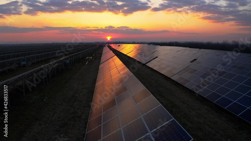 Flying from above Solar Power Station. Solar farm on the Field in Europe. Solar panels getting Clean energy from the Sun at Sunset. Green energy. Industrial Solar Energy Farm. Ecology concept 