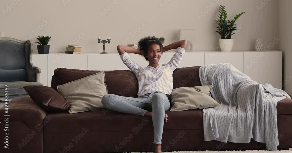 Smiling millennial multiracial woman resting on cozy sofa, daydreaming, breathing fresh air, visualizing future, enjoying mindful carefree weekend at home, satisfied with air conditioning system. Smiling millennial multiracial woman resting on cozy sofa, daydreaming, breathing fresh air, visualizing future, enjoying mindful carefree weekend at home, satisfied with air conditioning system.
