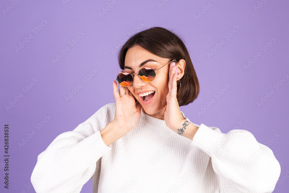 Young brunette in white casual sweater isolated on purple background wearing sunglasses happy smile positive moving Young brunette in white casual sweater isolated on purple background wearing sunglasses happy smile positive moving