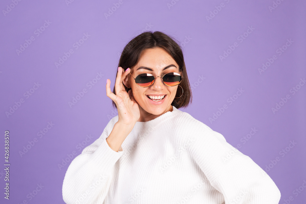 Young brunette in white casual sweater isolated on purple background wearing sunglasses happy smile positive moving Young brunette in white casual sweater isolated on purple background wearing sunglasses happy smile positive moving
