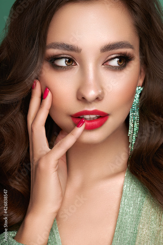 Portrait beautiful woman with jewelry. Brunette girl with long smooth hair. Beauty fashion. Model girl with red color manicure on nails in turquoise evening dress