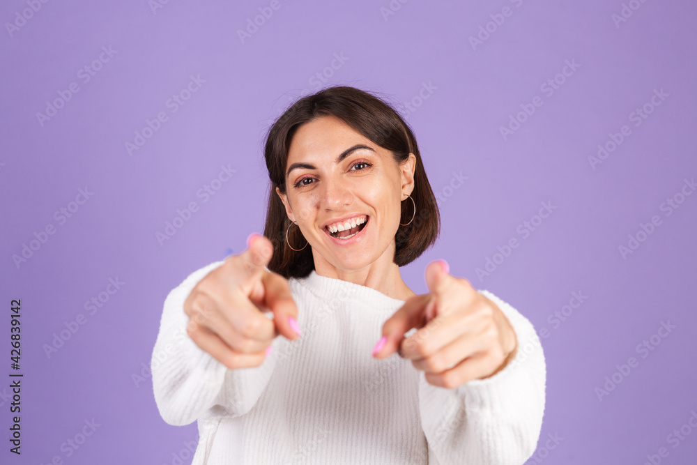 Young brunette in white casual sweater isolated on purple background point to you to camera with happy face Young brunette in white casual sweater isolated on purple background point to you to camera with happy face