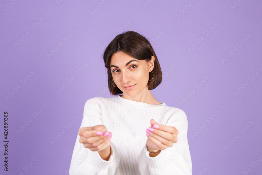 Young brunette in white casual sweater isolated on purple background rubbing fingers doing money gesture Young brunette in white casual sweater isolated on purple background rubbing fingers doing money gesture