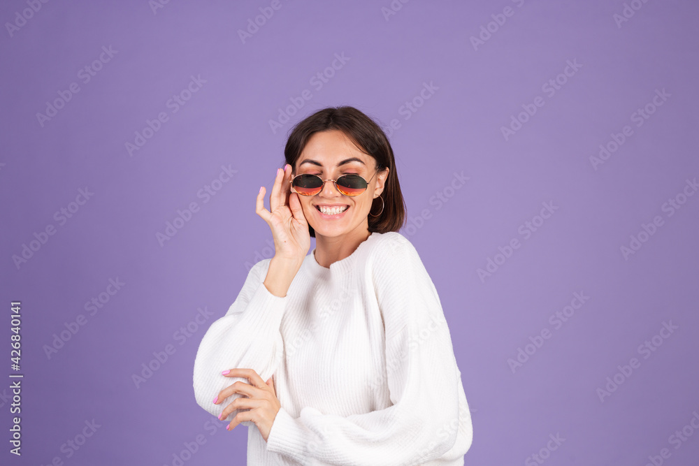 Young brunette in white casual sweater isolated on purple background in sunglasses happy stylish positive smiling Young brunette in white casual sweater isolated on purple background in sunglasses happy stylish positive smiling