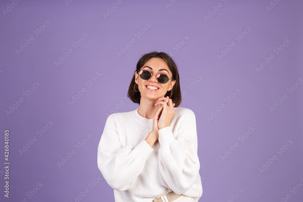 Young brunette in white casual sweater isolated on purple background in sunglasses happy stylish positive smiling Young brunette in white casual sweater isolated on purple background in sunglasses happy stylish positive smiling